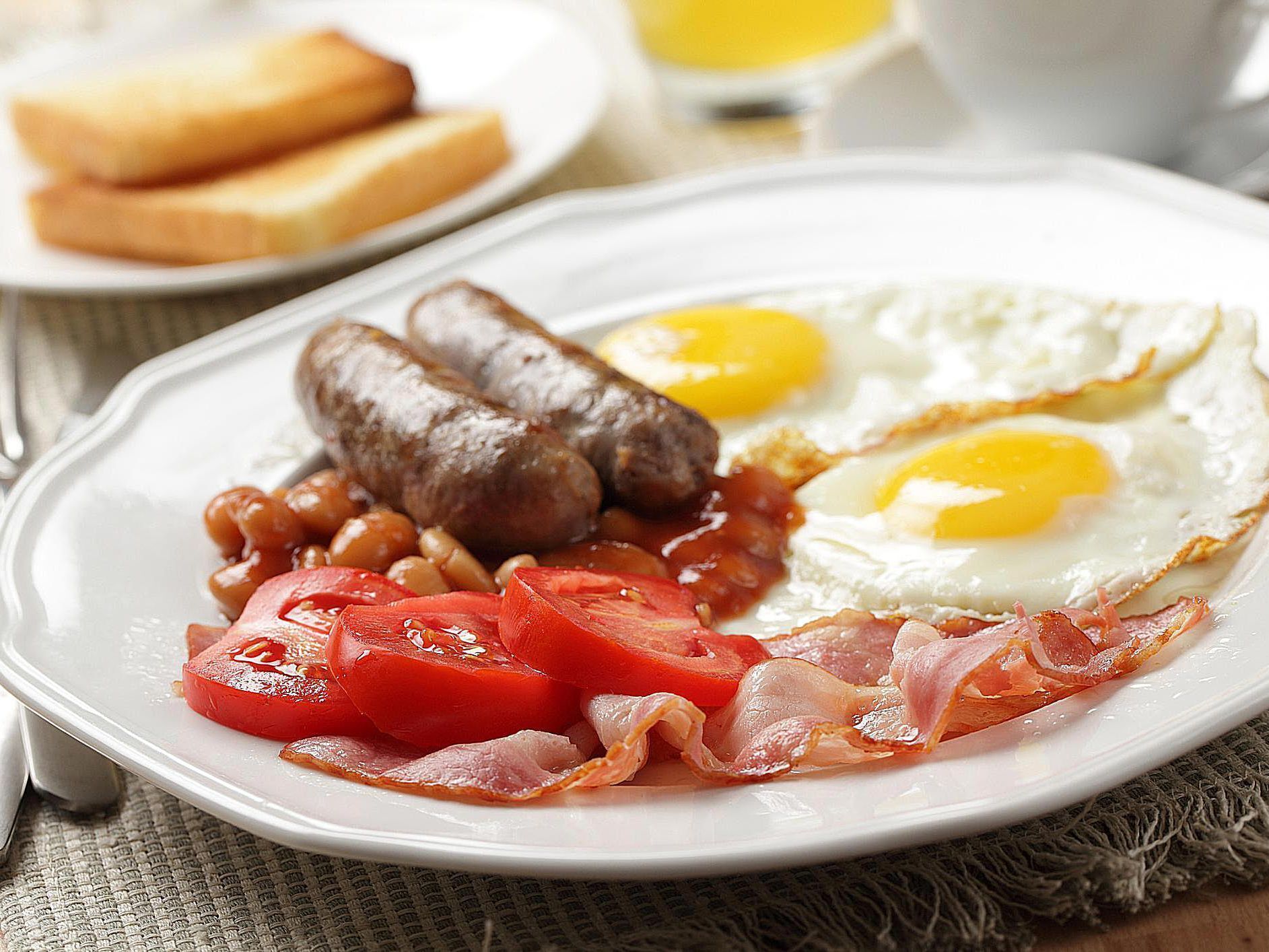 Un plato de comida para el desayuno con salchichas, huevos, frijoles, tomates y tocino.