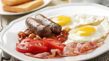 A plate of breakfast food including sausages, eggs, beans, tomatoes, and bacon.