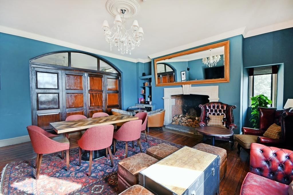 A room with a dining table, chairs, a fireplace, and a large mirror.
