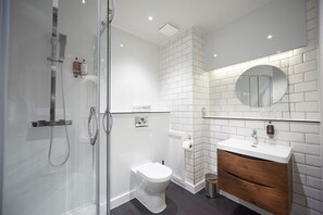 A modern bathroom with a glass shower enclosure, a white toilet, and a vanity with a wooden cabinet. - Chancellors Hotel and Conference Centre (Manchester)