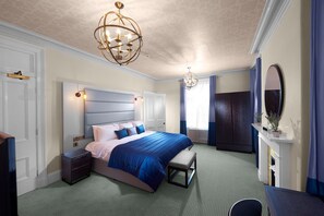 A bedroom with a large bed, a nightstand, a dresser, a mirror, and a chandelier. - Chancellors Hotel and Conference Centre (Manchester)