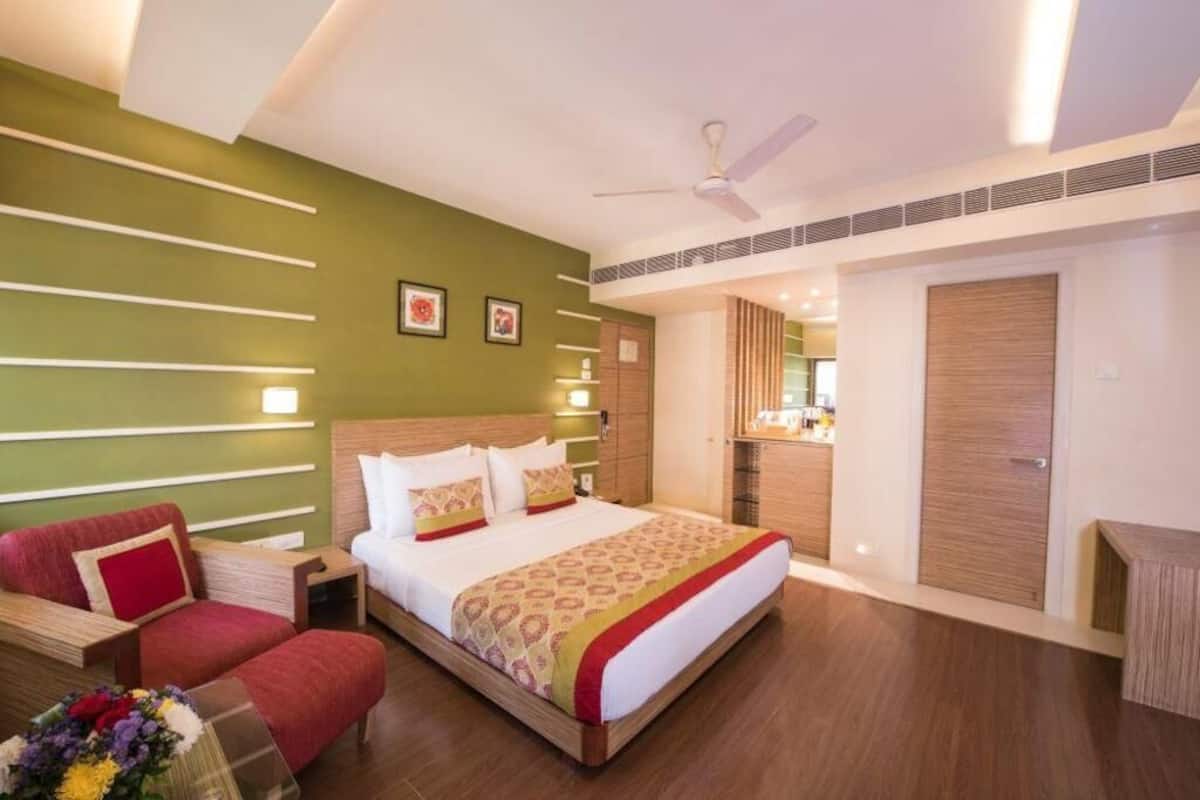Ein Hotelzimmer mit Bett, rotem Sessel, Nachttisch, Spiegel und Kleiderschrank.