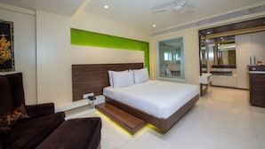 Ein modernes Hotelzimmer mit einem großen Bett, einer Couch, einem Schreibtisch und einem durch eine geöffnete Tür einsehbaren Badezimmer.