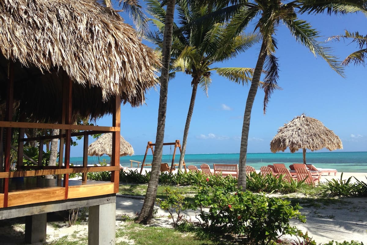 A beachside resort with thatched-roof structures, palm trees, and beach chairs.