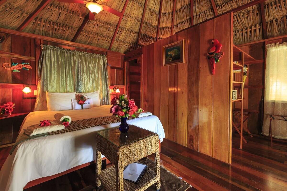 A wooden room with a bed, a small table, and a shelf with decorative items.