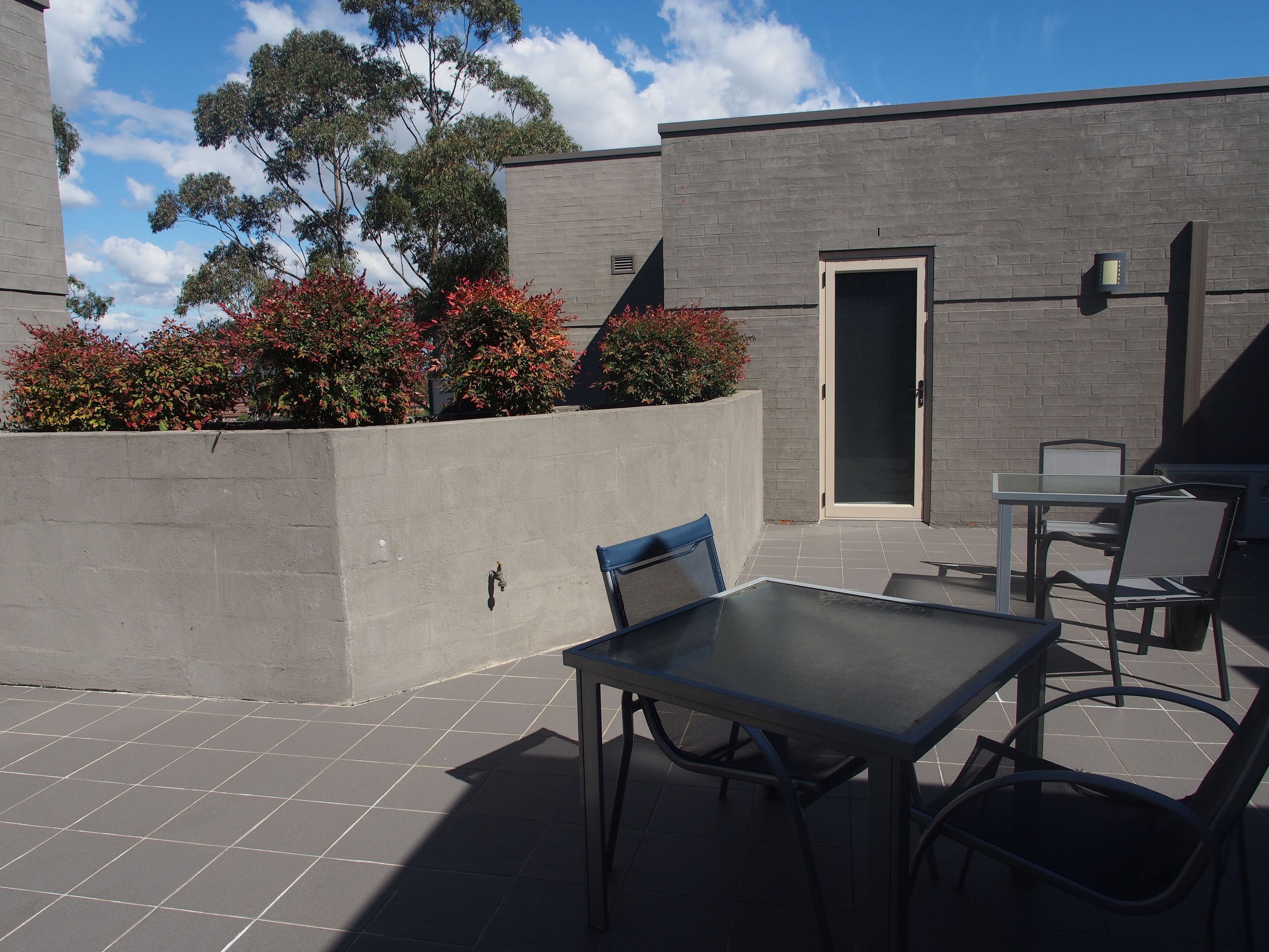 An outdoor patio area with a table and chairs, a concrete wall, and a door.
