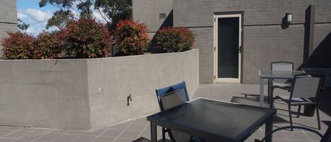 An outdoor patio area with a table and chairs, a concrete wall, and a door.