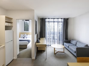 Ein Hotelzimmer mit Bett, Schreibtisch, Sofa, Fernseher und Kühlschrank.