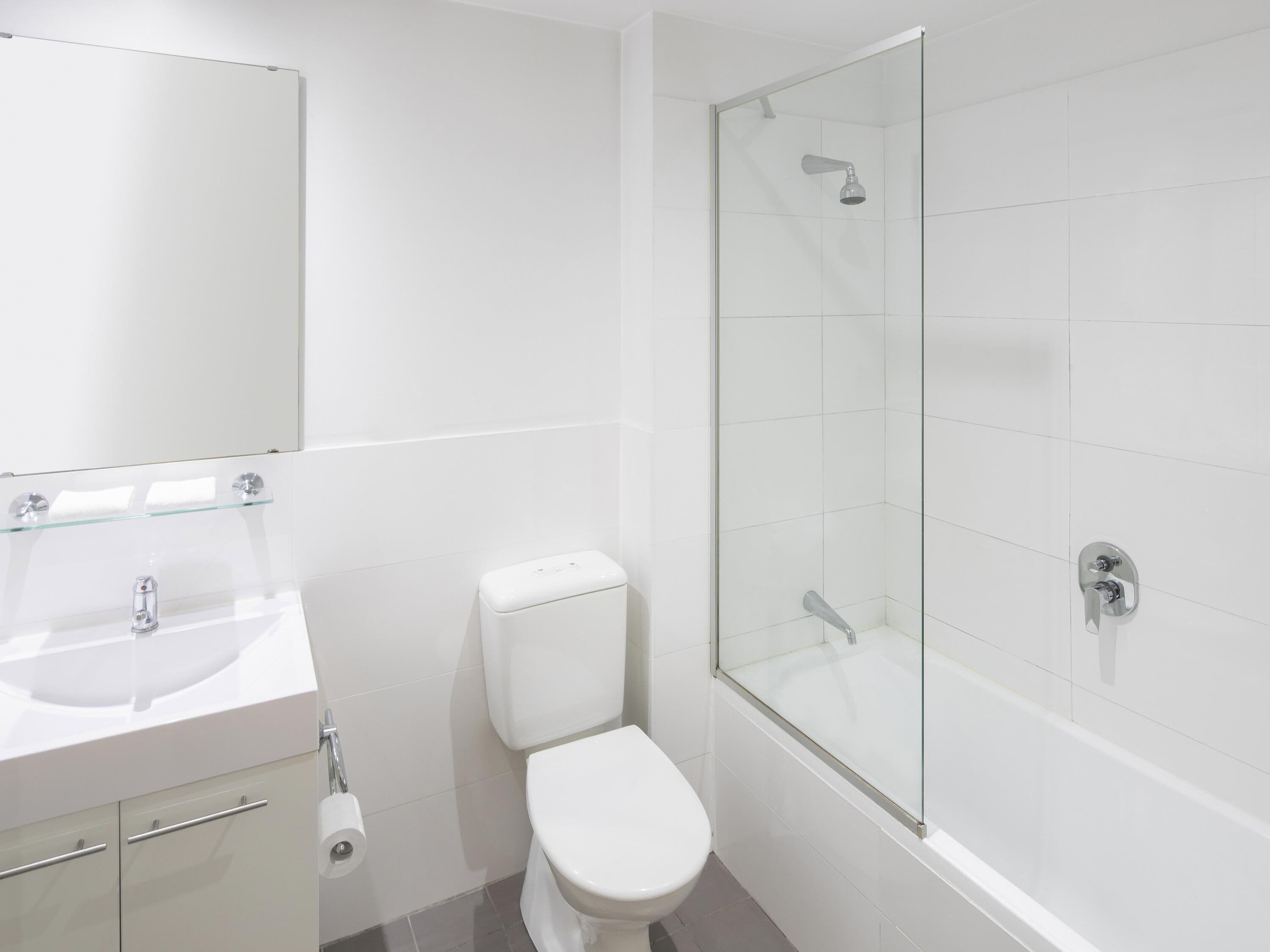 Een moderne badkamer met een douchecabine van glas, een wit toilet, een wastafel met spiegel en een toiletrolhouder.