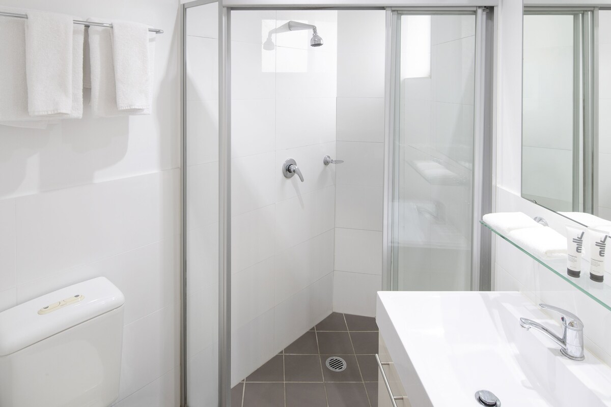 A modern bathroom with a glass-enclosed shower, a white sink with a glass shelf, and a toilet.