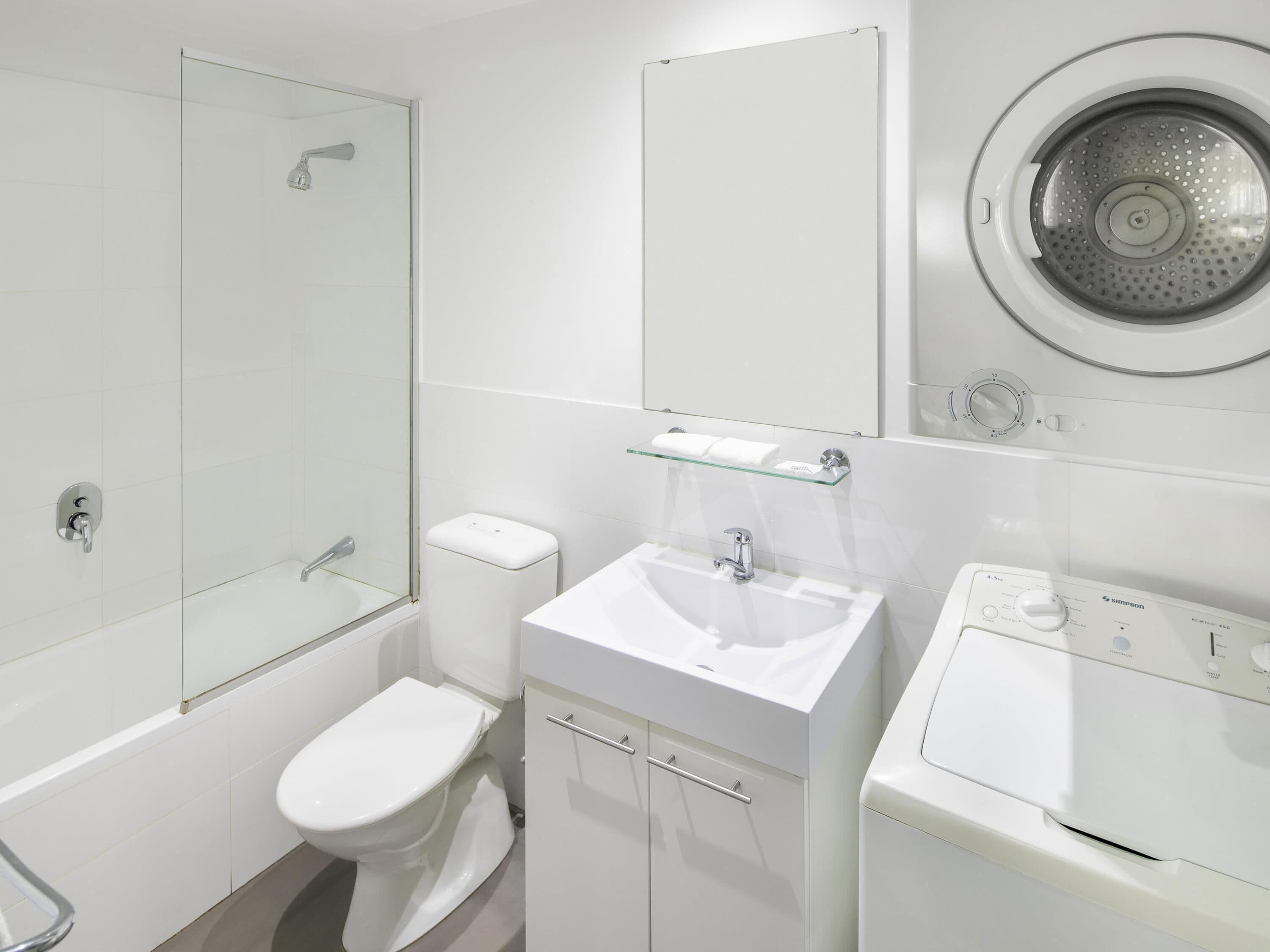 Un baño moderno con cabina de ducha de vidrio, inodoro, lavabo con espejo y lavadora de carga frontal.