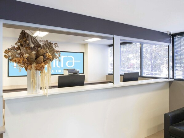 A reception desk with a large screen displaying 'THE HILL' and 'HILL'S HILL'. - Mantra Castle Hill Sydney (Castle Hill)