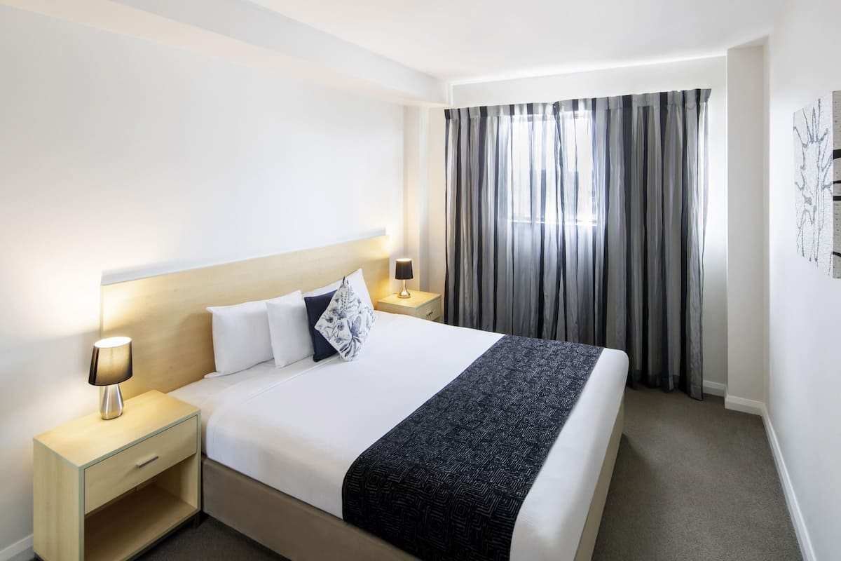 A hotel room with a bed, nightstand, lamp, and curtains.