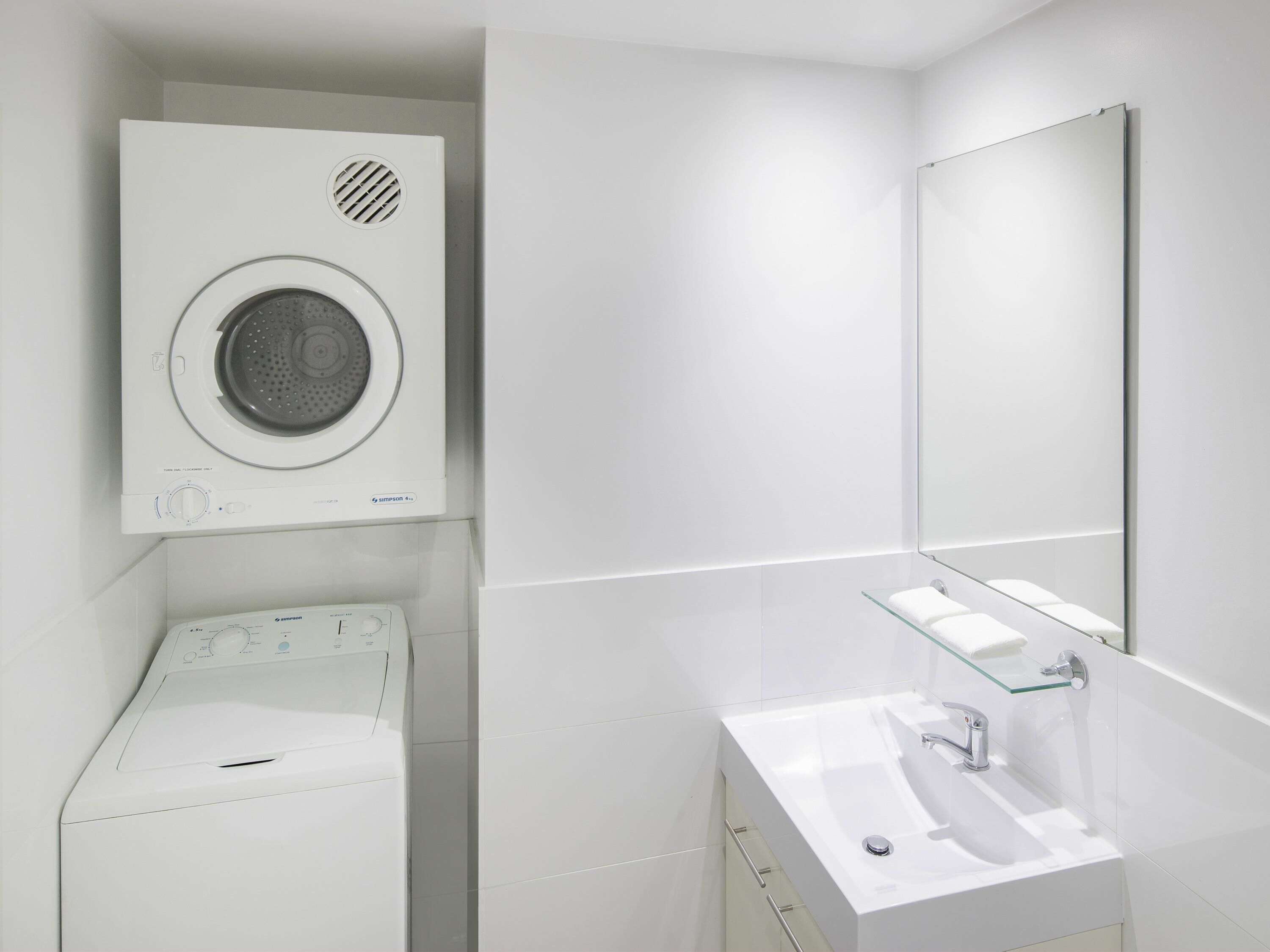 Un baño moderno con lavadora, repisa de vidrio y lavamanos.