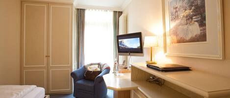Ein Hotelzimmer mit Bett, Schreibtisch mit Computer, Stuhl, Lampe und einem gerahmten Bild an der Wand.