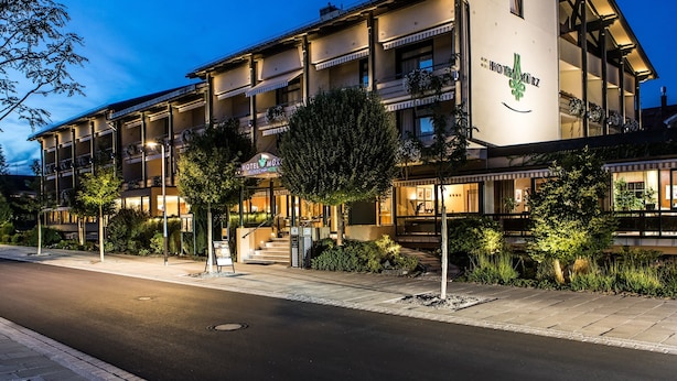 Un hotel de varios pisos con un logotipo destacado en la fachada, zona de estar al aire libre y una entrada bien iluminada.