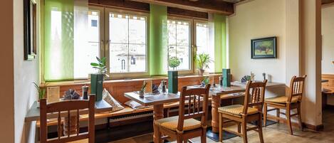 A restaurant with wooden tables and benches, large windows with green curtains, and a wooden ceiling.