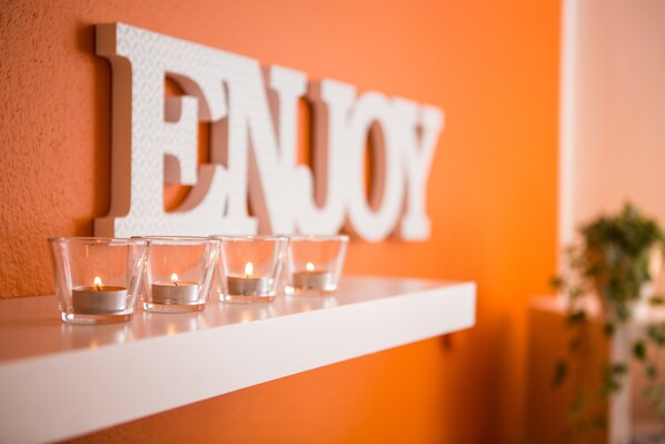 A white shelf with three lit candles and a large "ENJOY" sign on an orange wall.