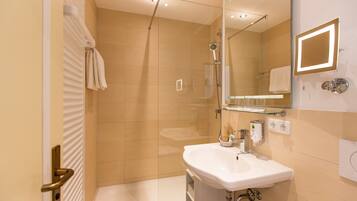 Un bany modern amb un compartiment de dutxa de vidre, un lavabo blanc i un mirall amb il·luminació incrustada.