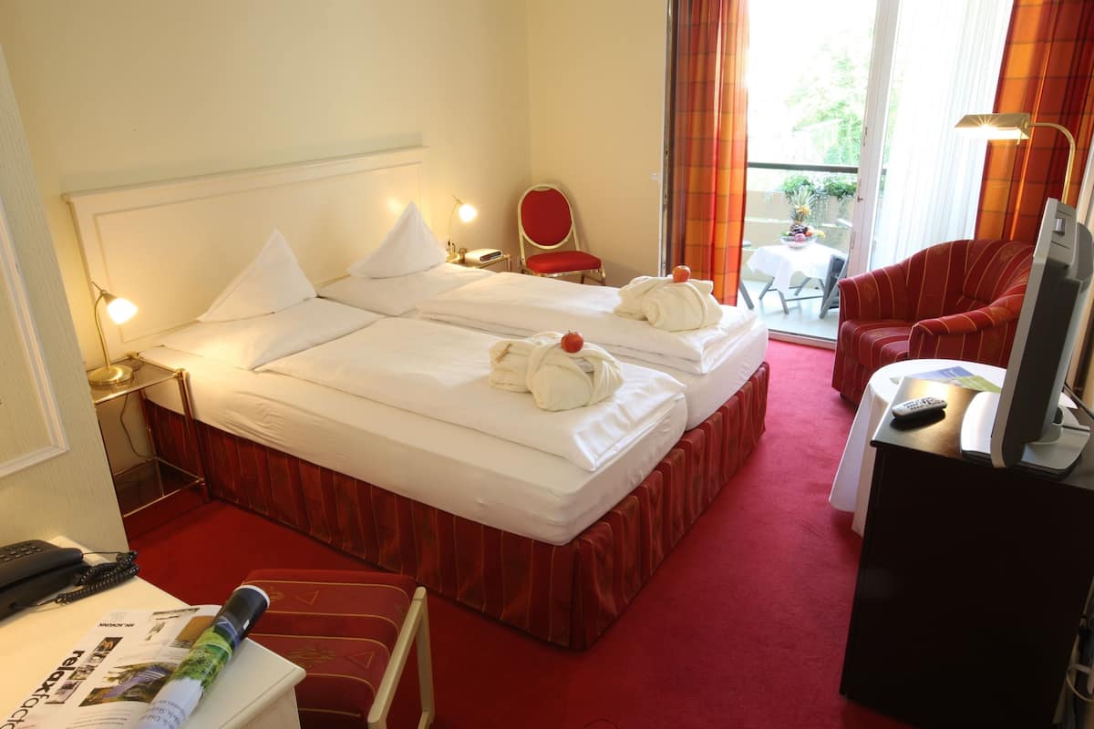 A hotel room with two beds, a TV, a desk with a remote, and a chair.