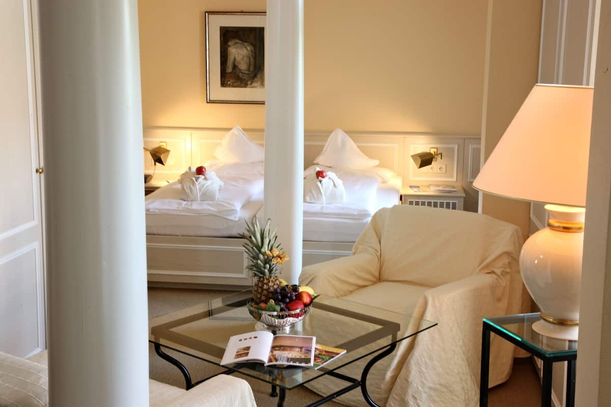 A hotel room with a bed, a sofa, a coffee table with a fruit bowl and magazine, and a lamp.