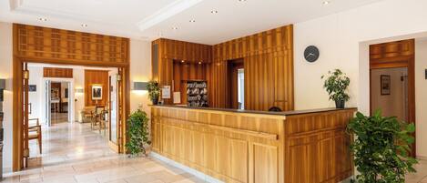 A reception area with a wooden reception desk, a clock on the wall, and potted plants.