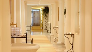 Un pasillo de hotel con piso de mármol, una bañera y un expositor de vidrio.