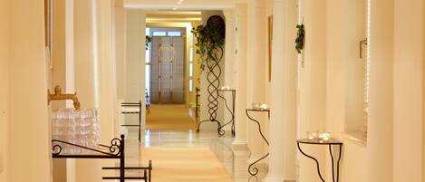 A hotel hallway with a marble floor, a bathtub, and a glass display case.