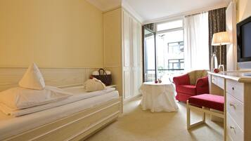 A hotel room with a bed, a small table, a red chair, a TV, and a window with curtains.