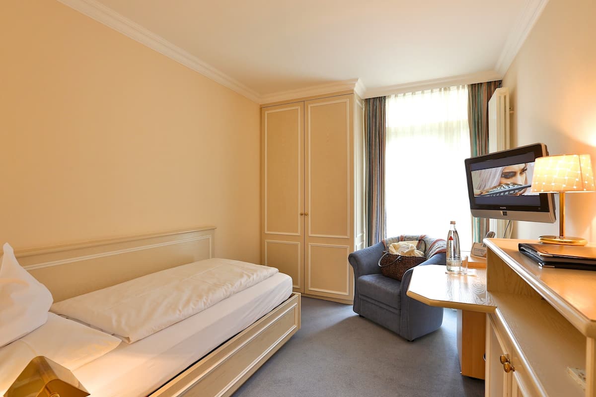 A hotel room with a bed, a desk with a computer, a chair, and a TV.