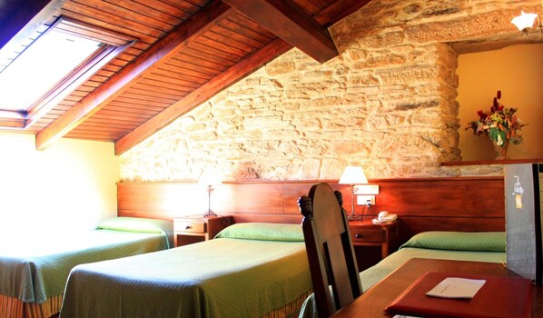 A room with two single beds, wooden beams, a stone wall, and a small table with a lamp. - Hostal San Clemente by Pousadas de Compostela (Santiago de Compostela)