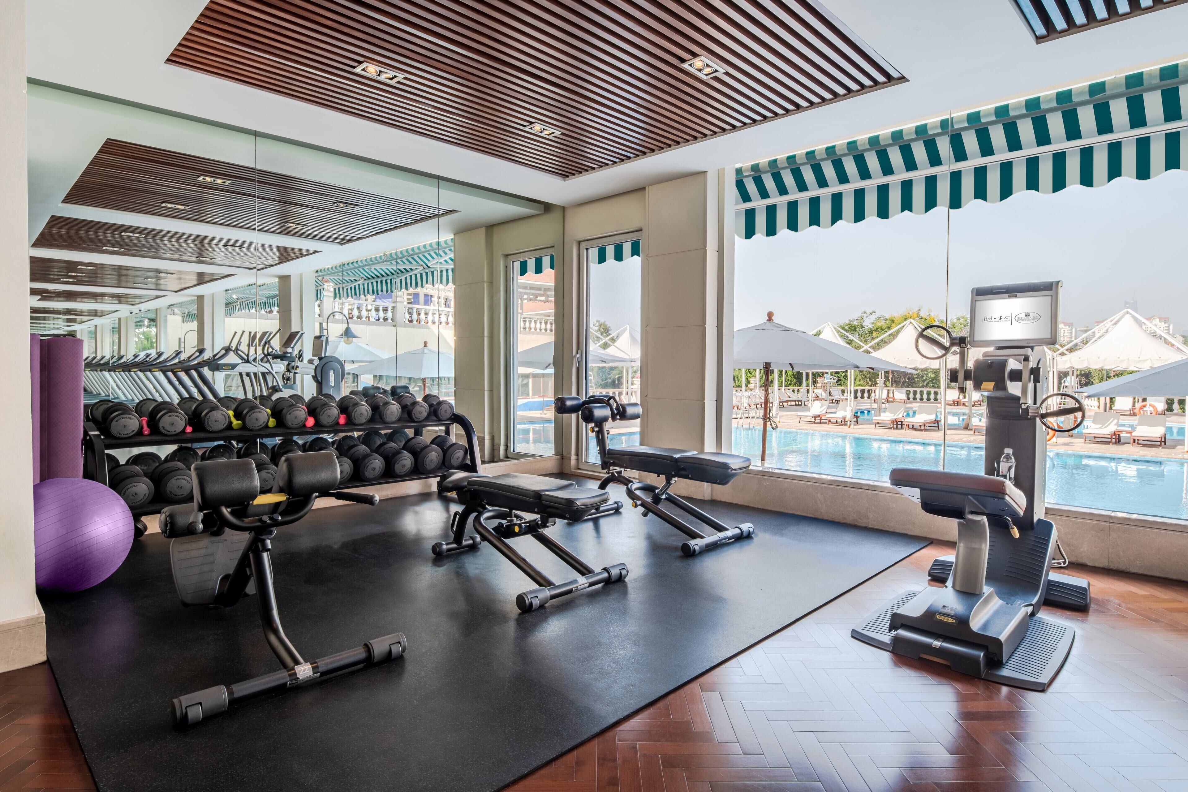 A gym with exercise equipment, a weight rack, and a view of a pool and buildings.