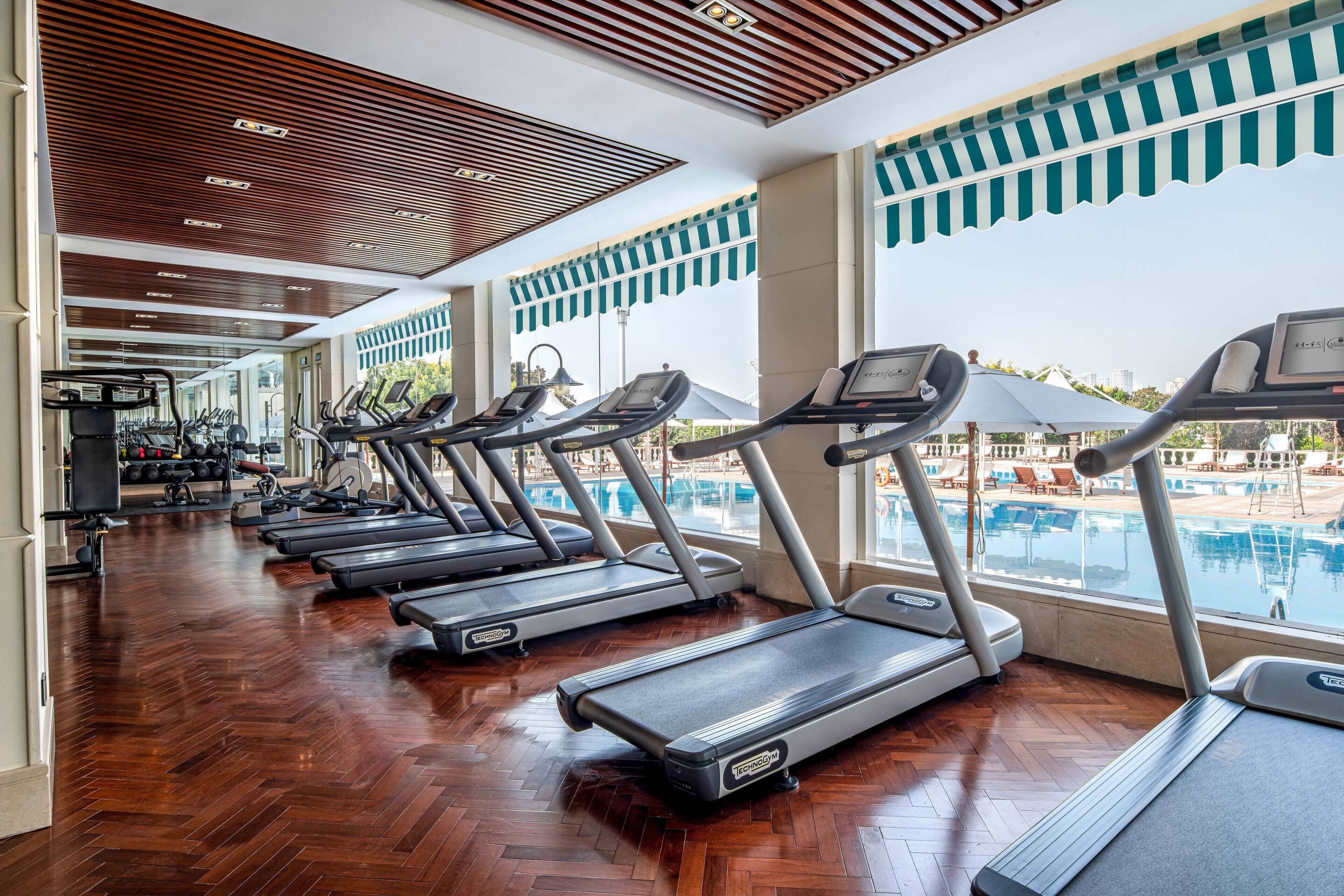 A gym with treadmills, wooden flooring, and a view of a swimming pool.