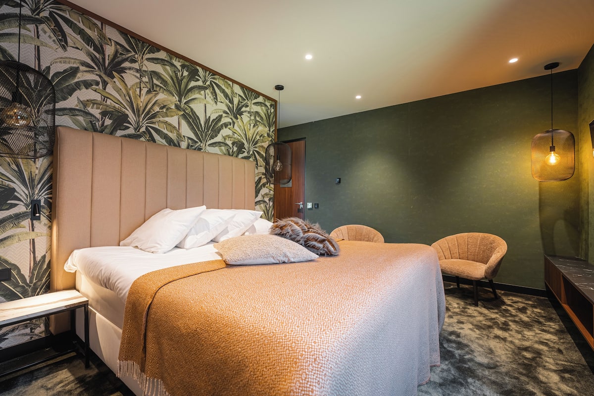 A hotel room with a large bed, a chair, a nightstand, and a wall with a tropical wallpaper.