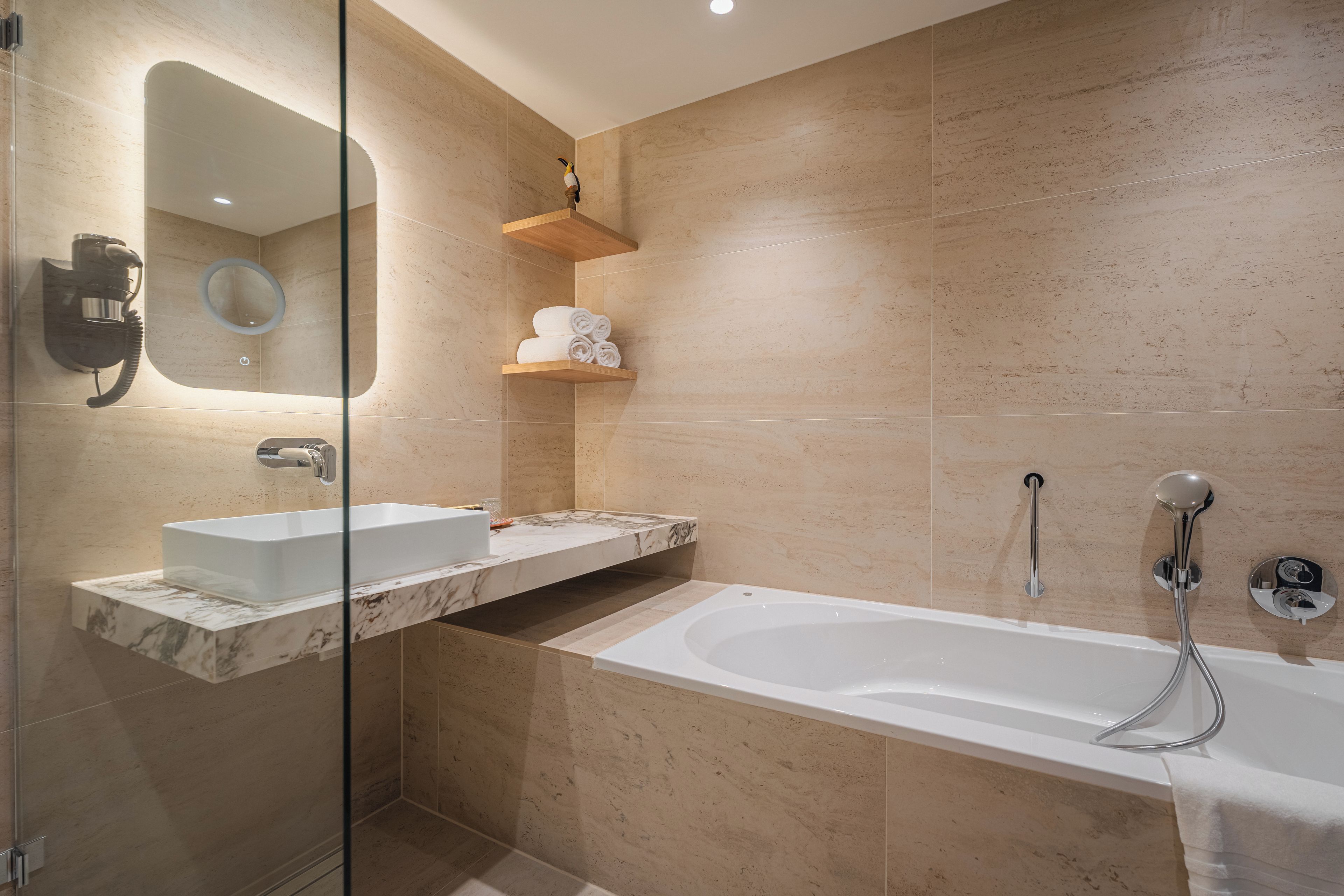 Un baño moderno con ducha envuelta en vidrio, una bañera blanca y un encimera de mármol con un lavamanos.
