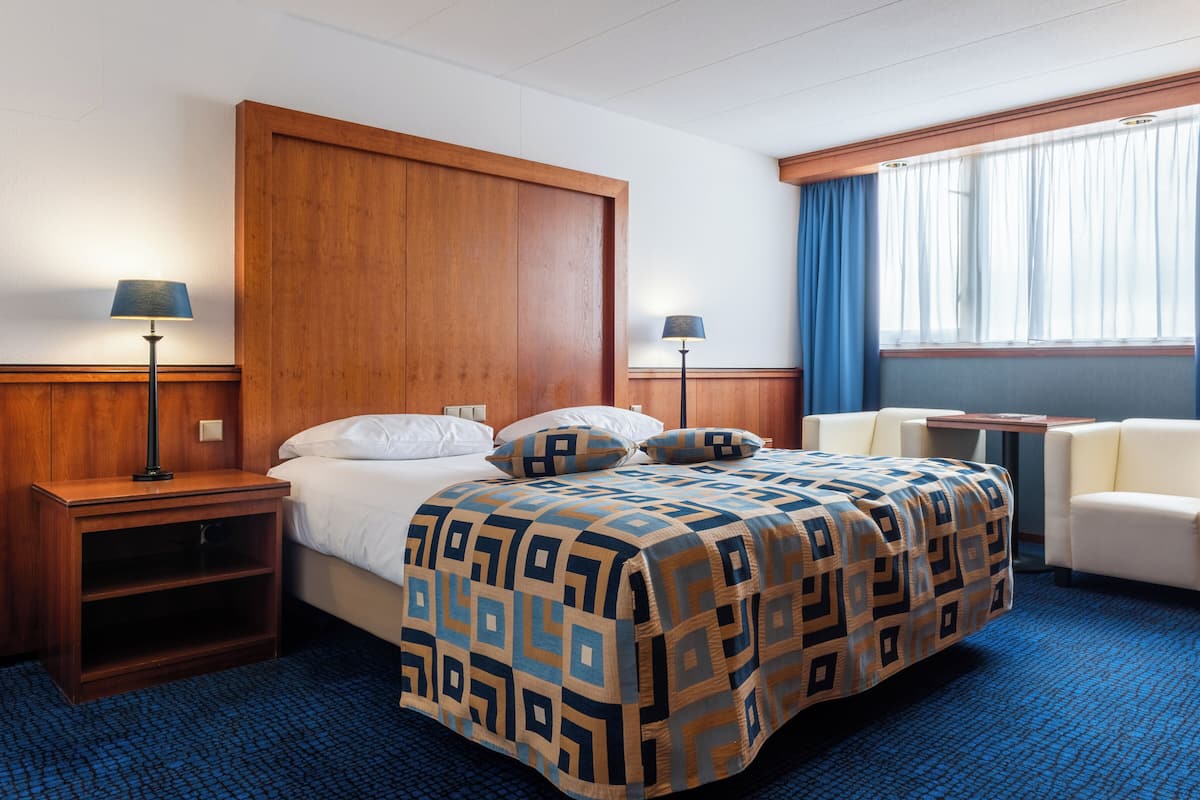 A hotel room with a bed, two bedside tables, a desk, a chair, and a window with curtains.