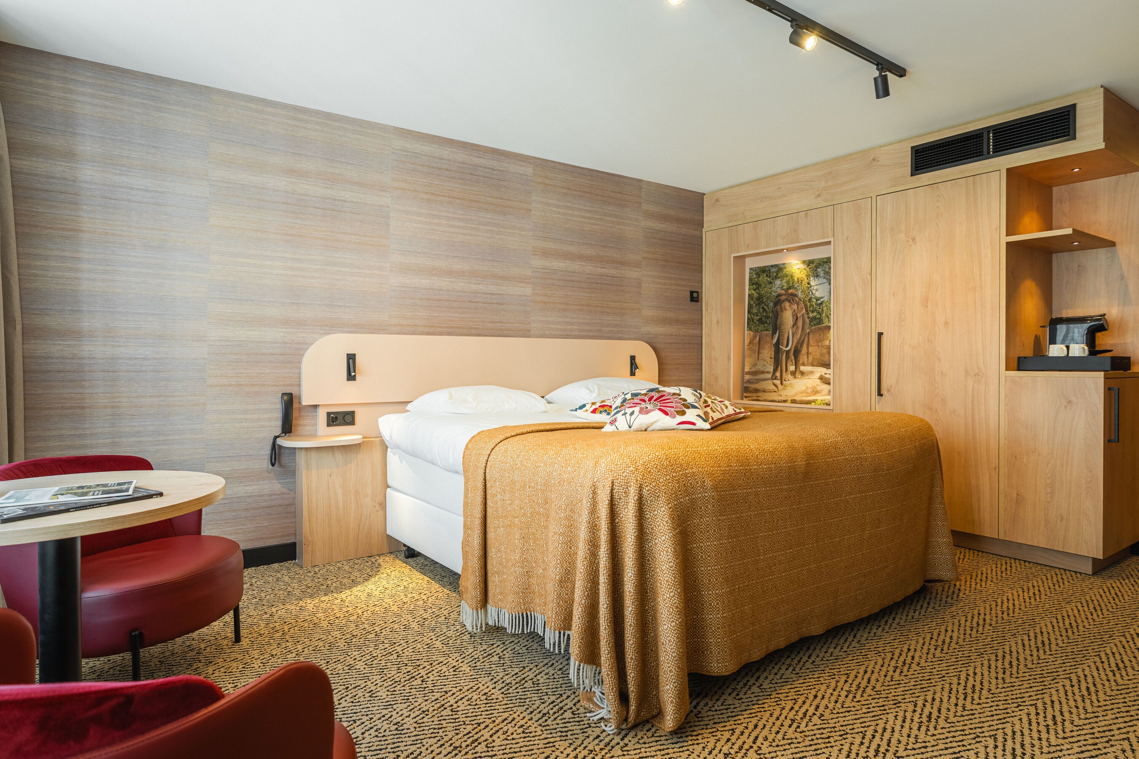 Een hotelkamer met een bed, bureau, stoel, klein tafeltje en kast.