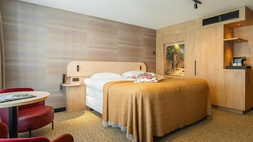 Una habitación de hotel con cama, escritorio, silla, mesita y armario.