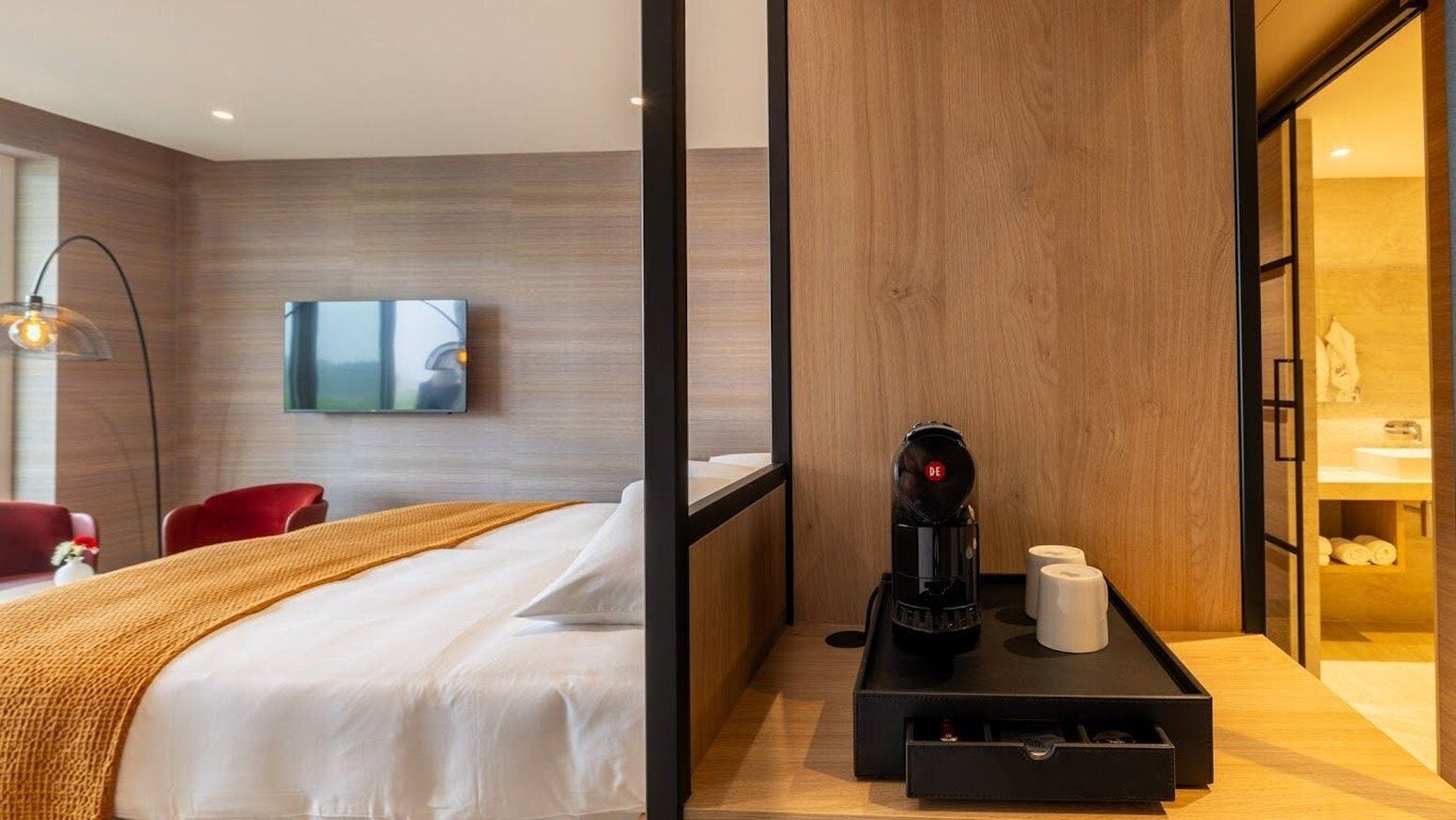 A hotel room with a bed, a coffee maker, a TV, and a wooden wall.