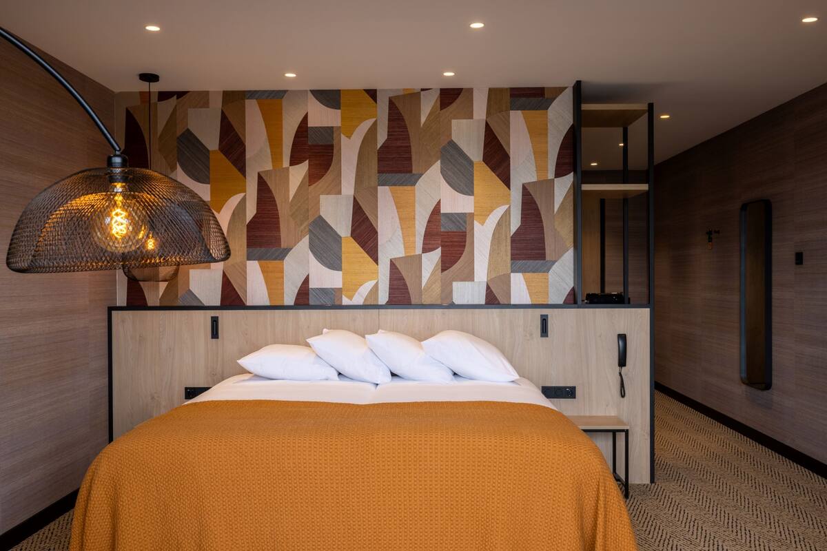 A modern hotel room with a large bed, a patterned wall, and a hanging lamp.