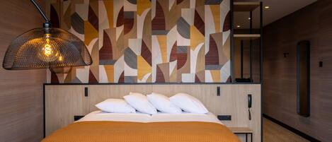 A modern hotel room with a large bed, a patterned wall, and a hanging lamp.