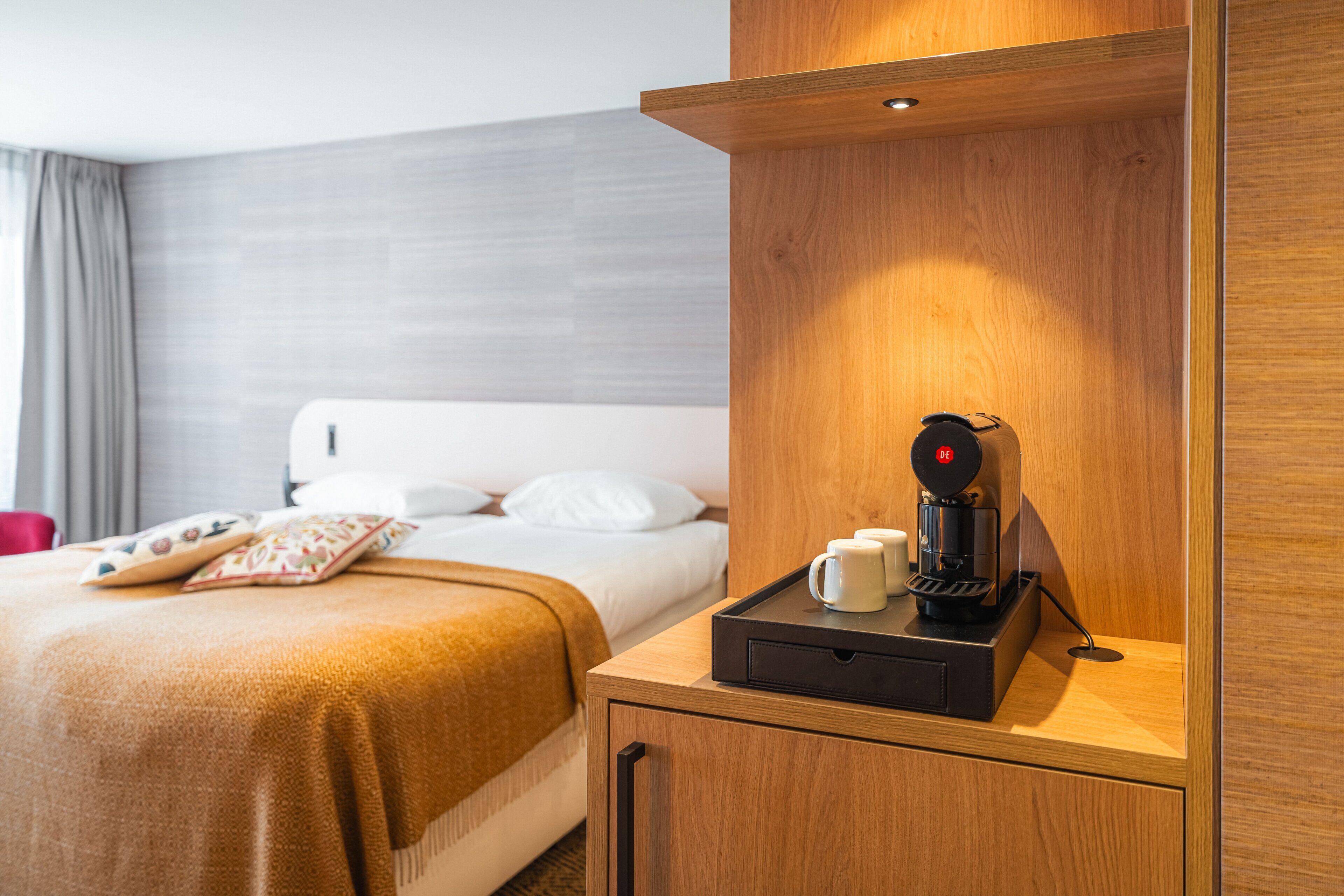 A hotel room with a bed, a bedside table with a coffee maker, and a wooden headboard.