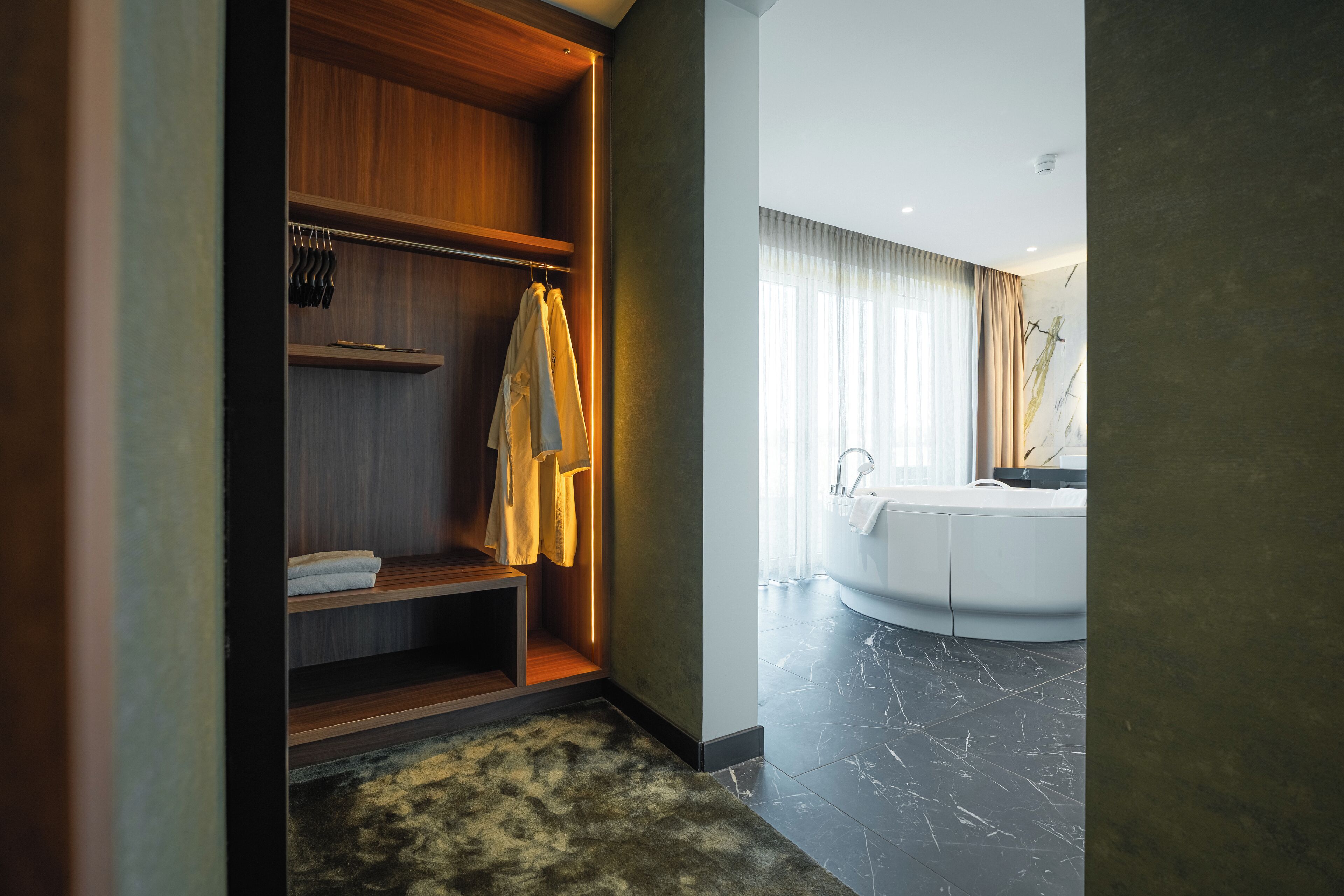 A modern bathroom with a freestanding bathtub, wooden shelving, and a fluffy rug.