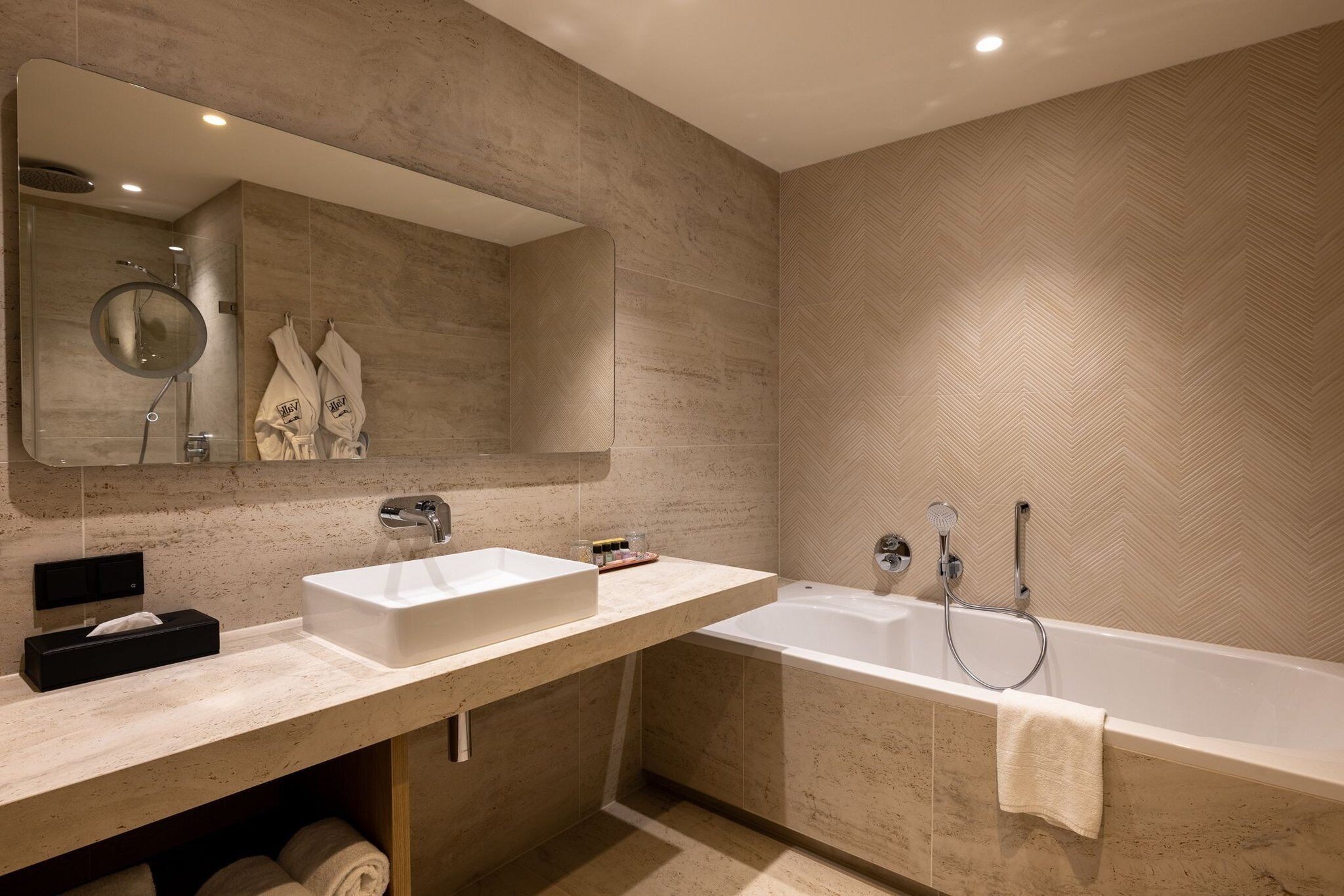A modern bathroom with a large mirror, two sinks, a bathtub, and towels.