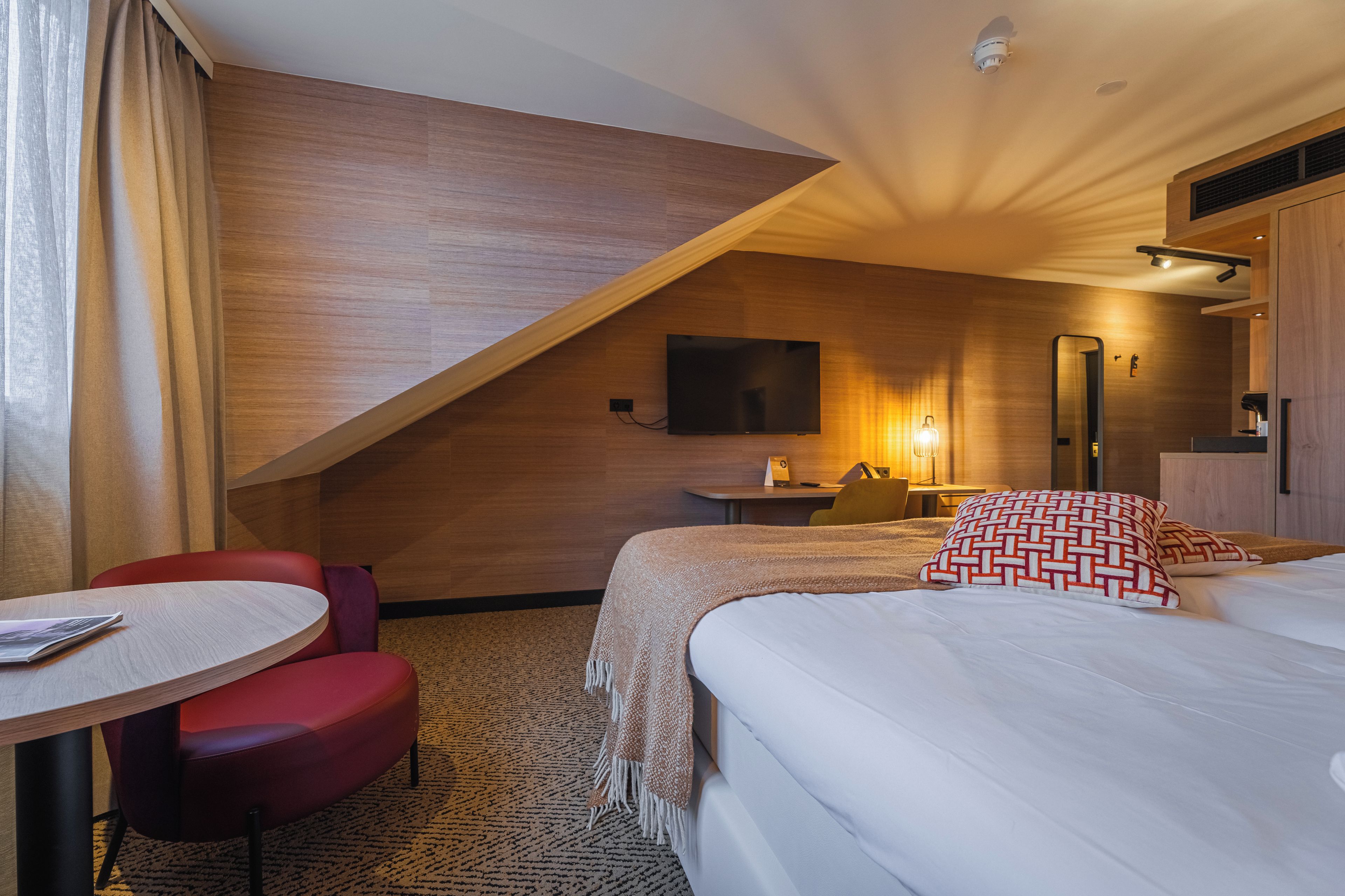 A hotel room with a bed, a desk, a chair, a television, and a mirror.