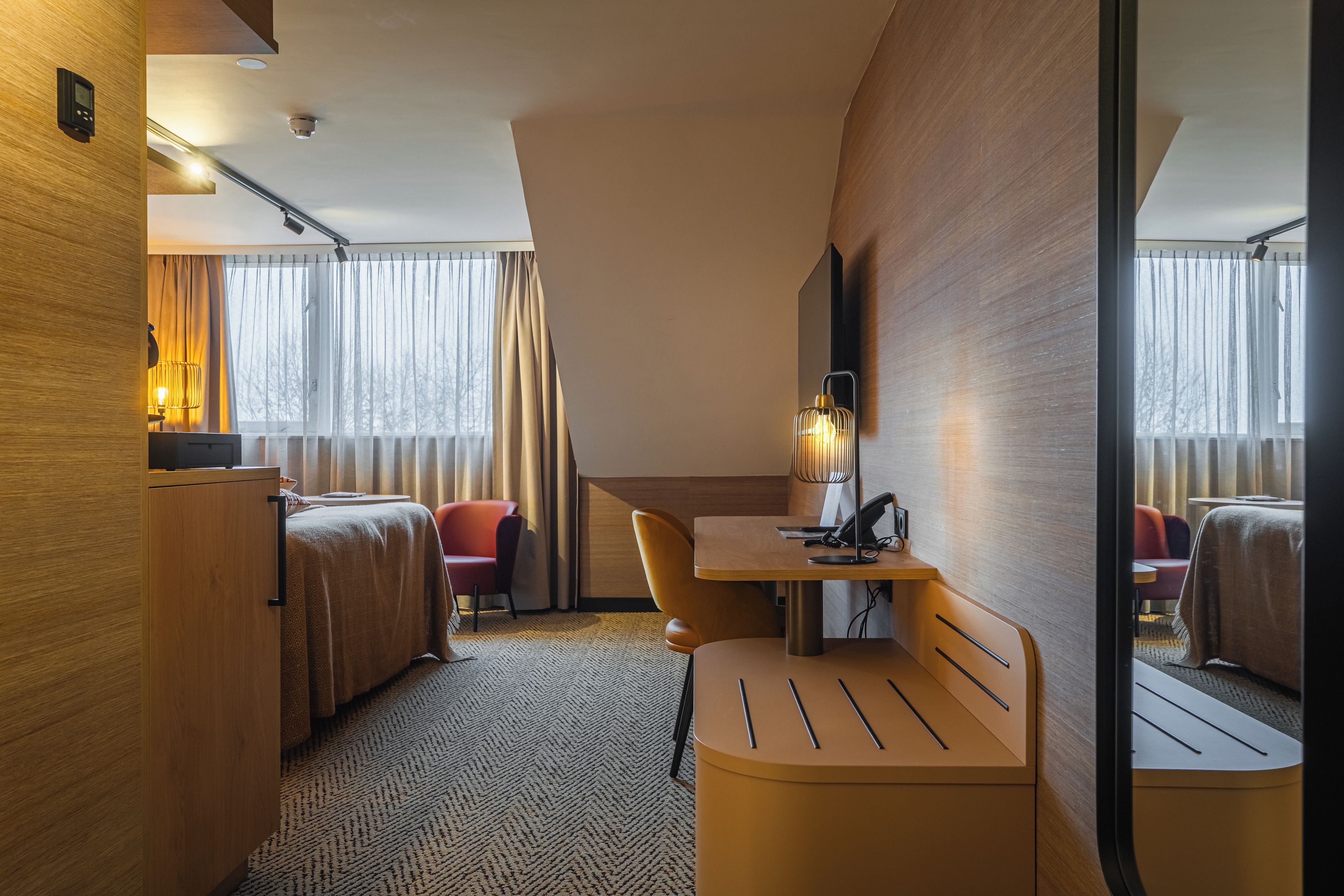 Una habitación de hotel con cama, escritorio, silla, lámpara y espejo.
