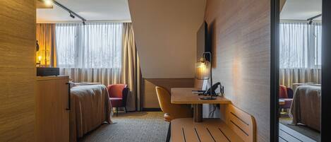 Quarto de hotel com cama, escrivaninha, cadeira, luminária e espelho.