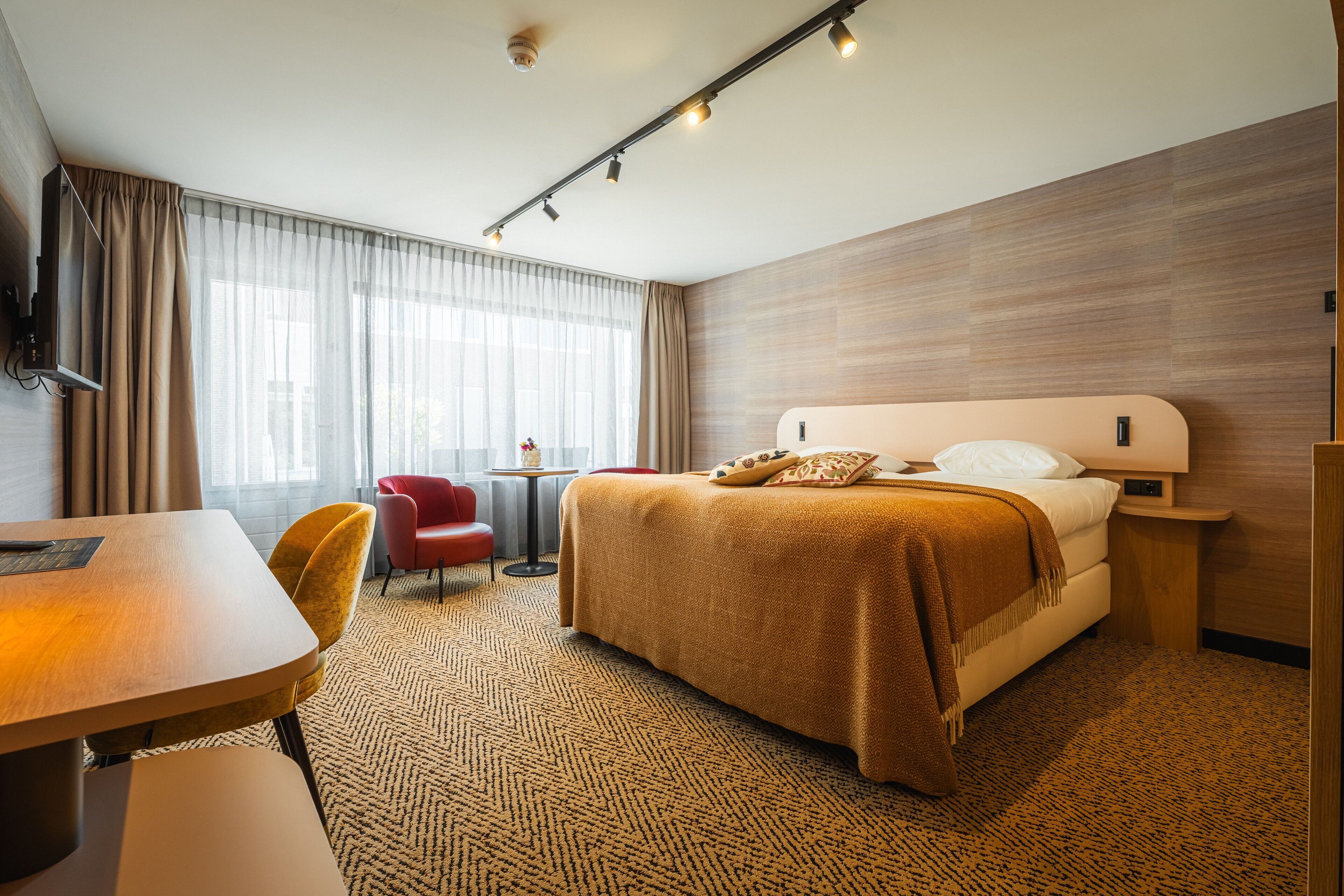 A hotel room with a bed, a desk, a chair, and a small table.