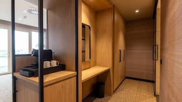 A modern hotel room with a wooden interior, a desk with a coffee machine, and a large mirror.
