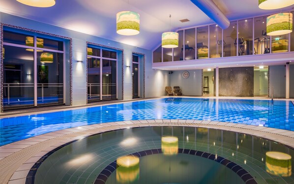 An indoor swimming pool with clear blue water, surrounded by walls with large windows and a modern ceiling design.